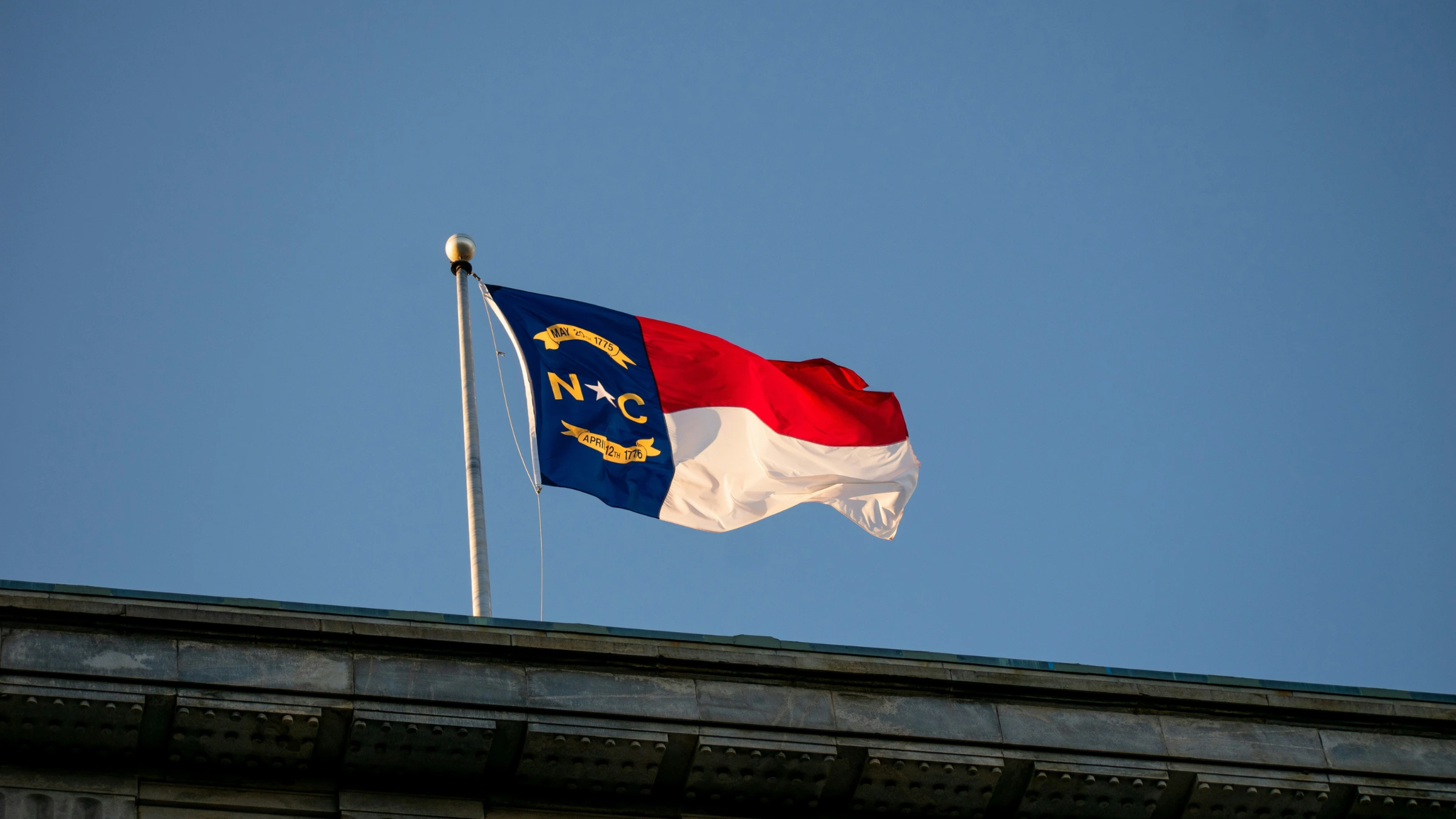 North Carolina state flag displayed above public building against clear blue sky