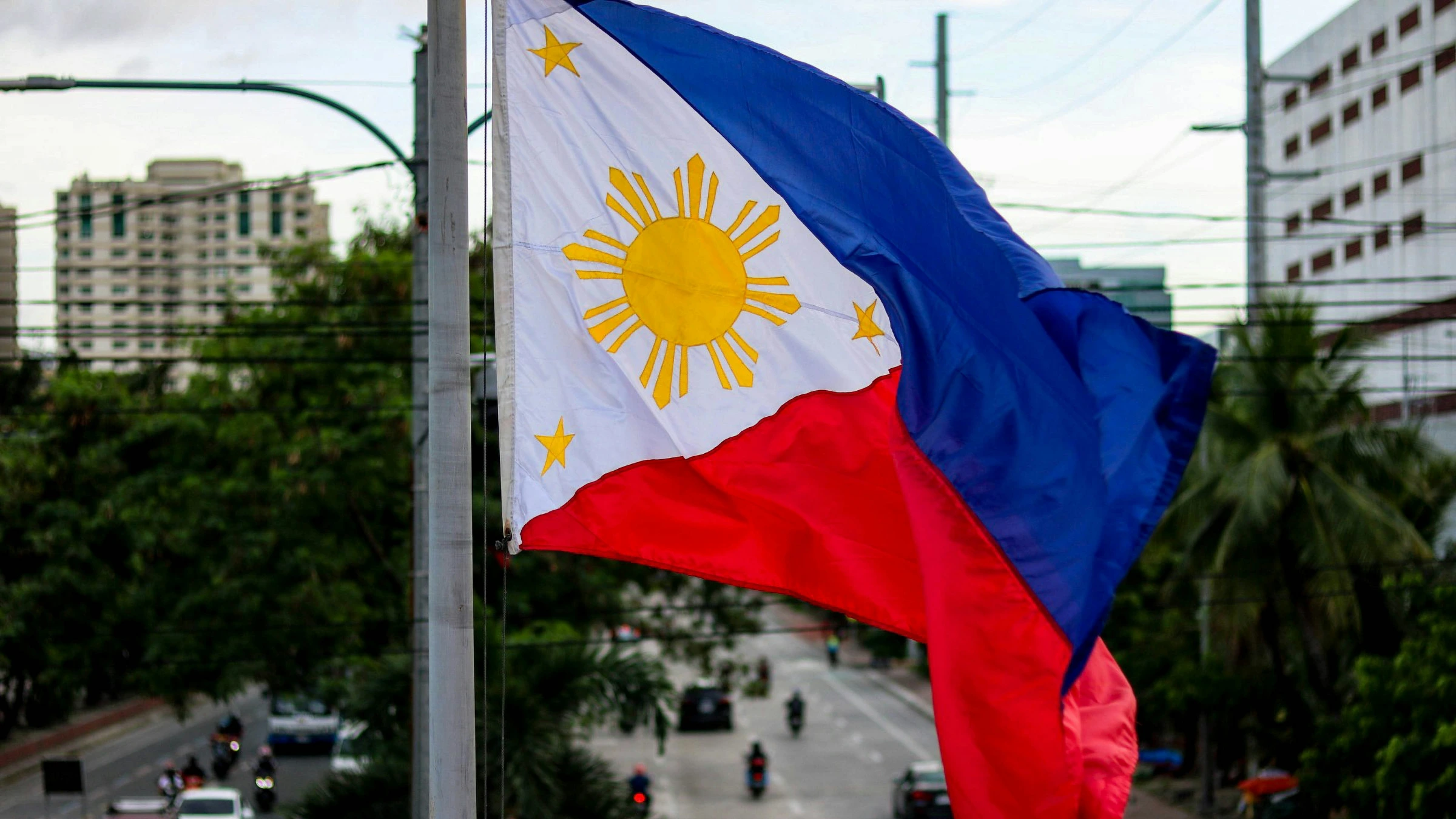 Philippine national flag waving over an urban city roadway