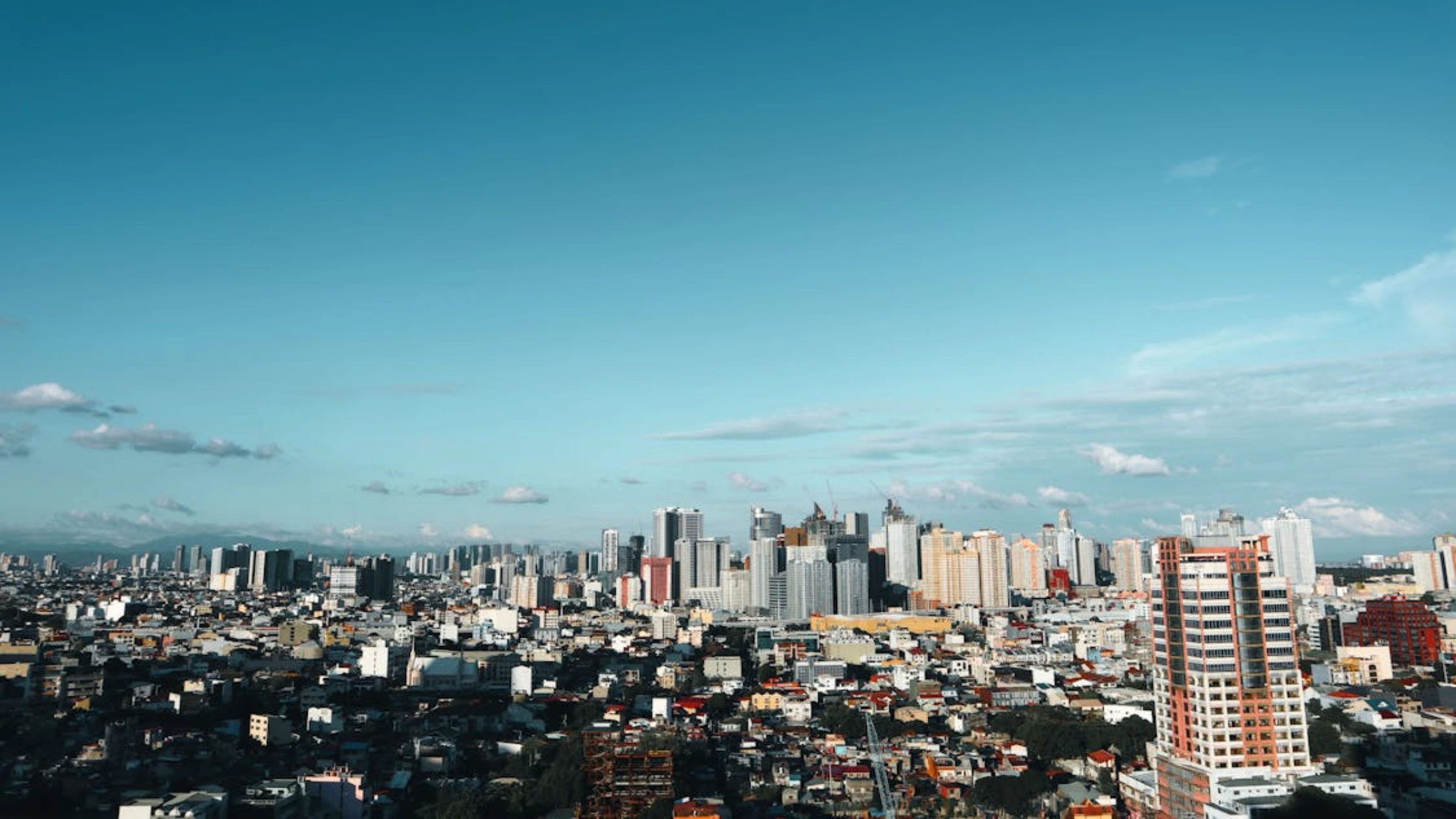 Wide city skyline with dense buildings under blue sky and scattered clouds.