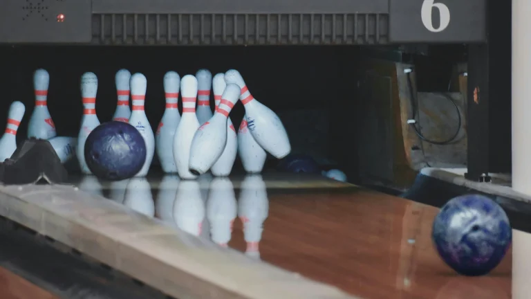 Bowling ball rolls toward a cluster of pins on a polished lane inside a bowling alley.