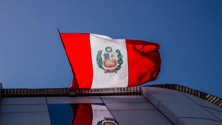 Peruvian national flag flying above building rooftop against clear blue sky