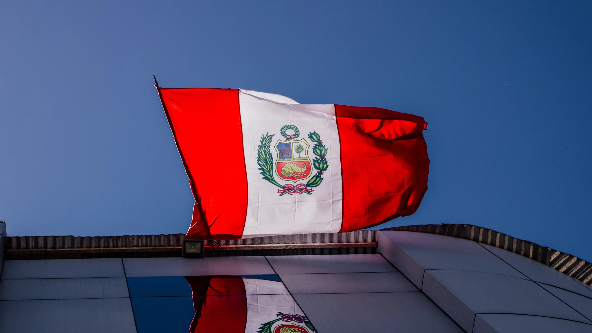 Peruvian national flag flying above building rooftop against clear blue sky