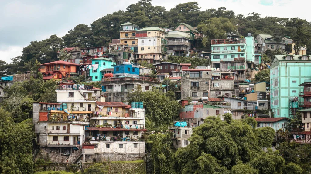 Dense hillside neighborhood with colorful multi-story houses surrounded by trees and vegetation.