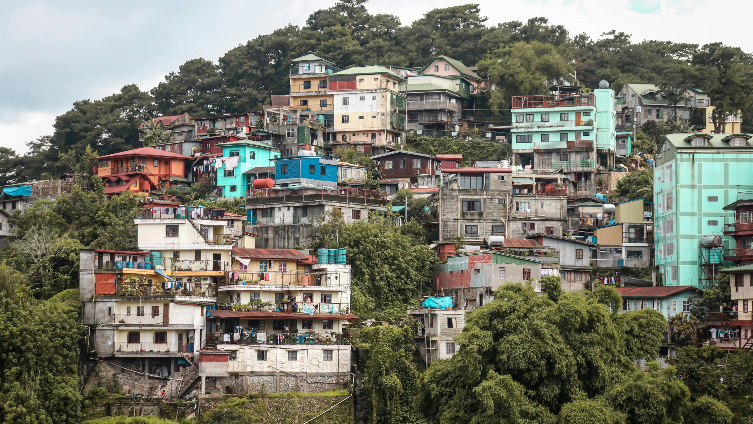 Dense hillside neighborhood with colorful multi-story houses surrounded by trees and vegetation.