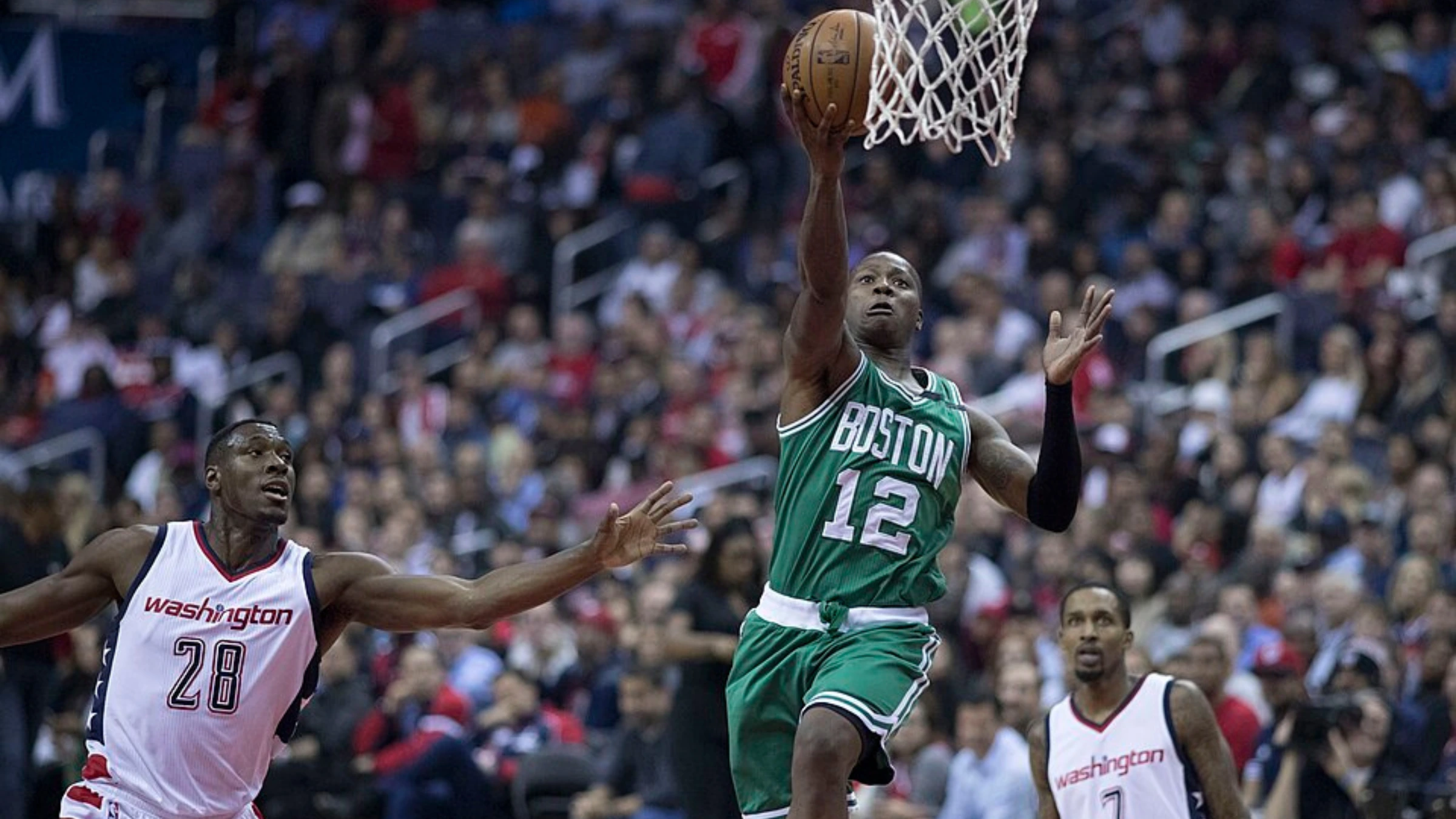 Basketball player drives to basket during professional game action before crowd