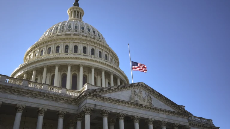United States Capitol building with American flag flying against a clear blue sky