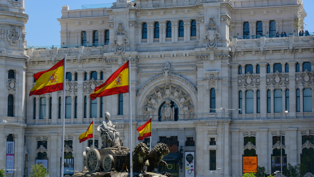 Spanish flags fly in front of ornate historic government building with statues and decorative