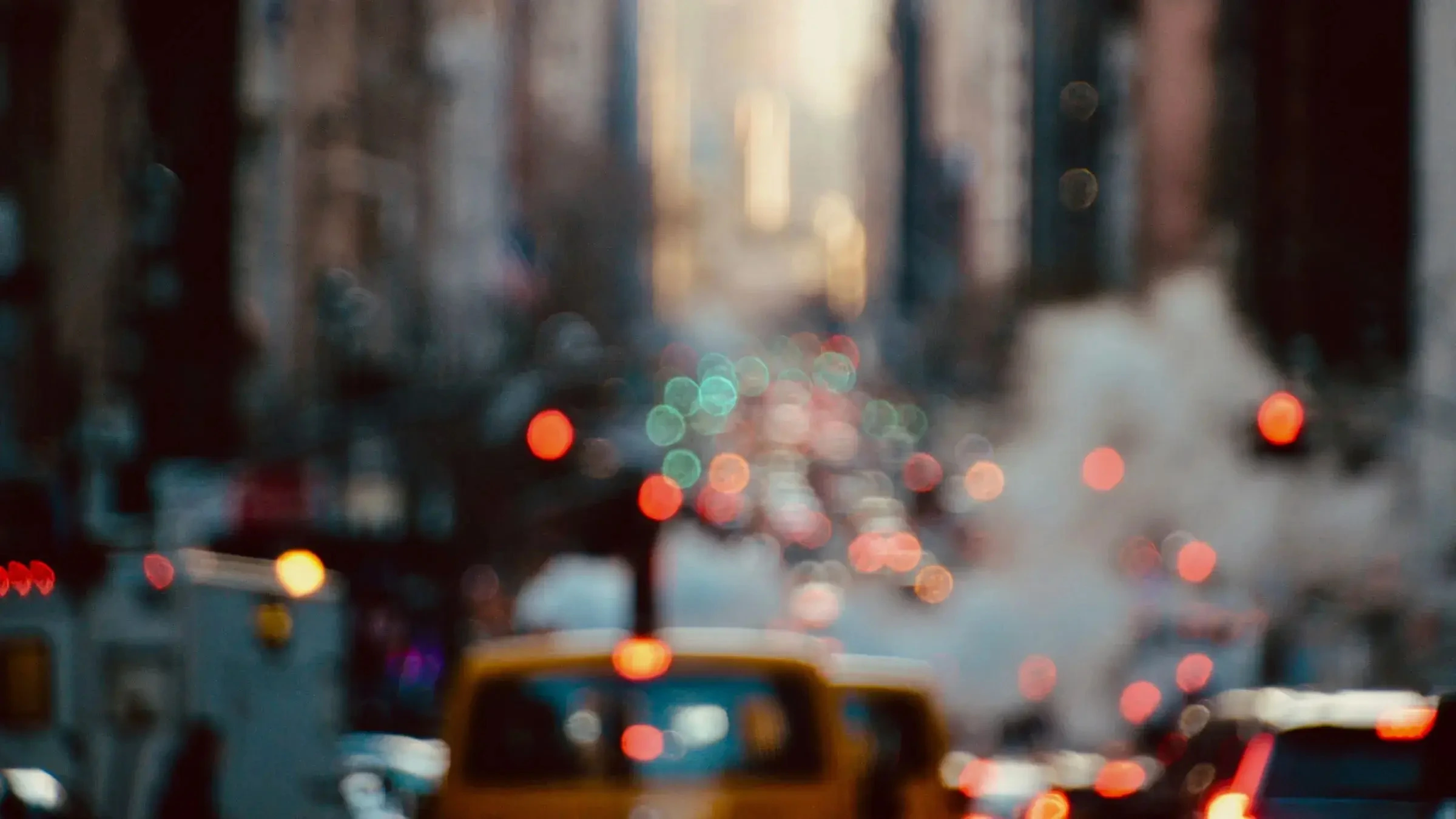 Blurred city street with traffic lights, cars, and steam rising between buildings.