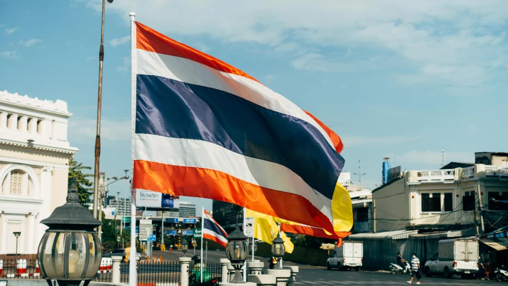 Thai national flag flying above city street with buildings and traffic nearby