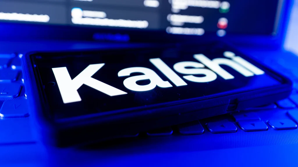 Kalshi logo displayed on smartphone screen with laptop keyboard in background