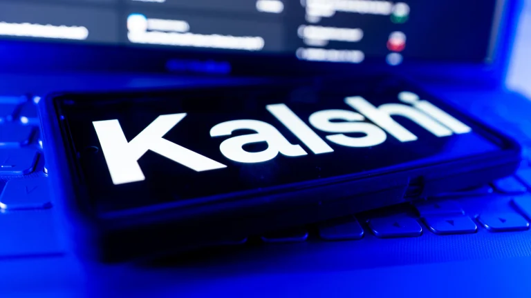 Kalshi logo displayed on smartphone screen with laptop keyboard in background