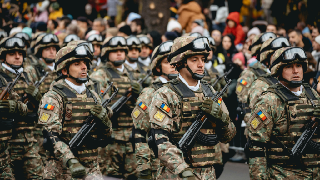 Soldiers in camouflage uniforms march in formation holding rifles during a public military parade.