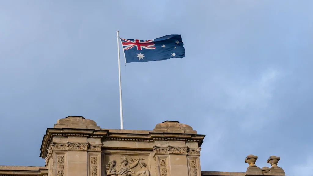 Australian national flag flying above historic government building under clear sky