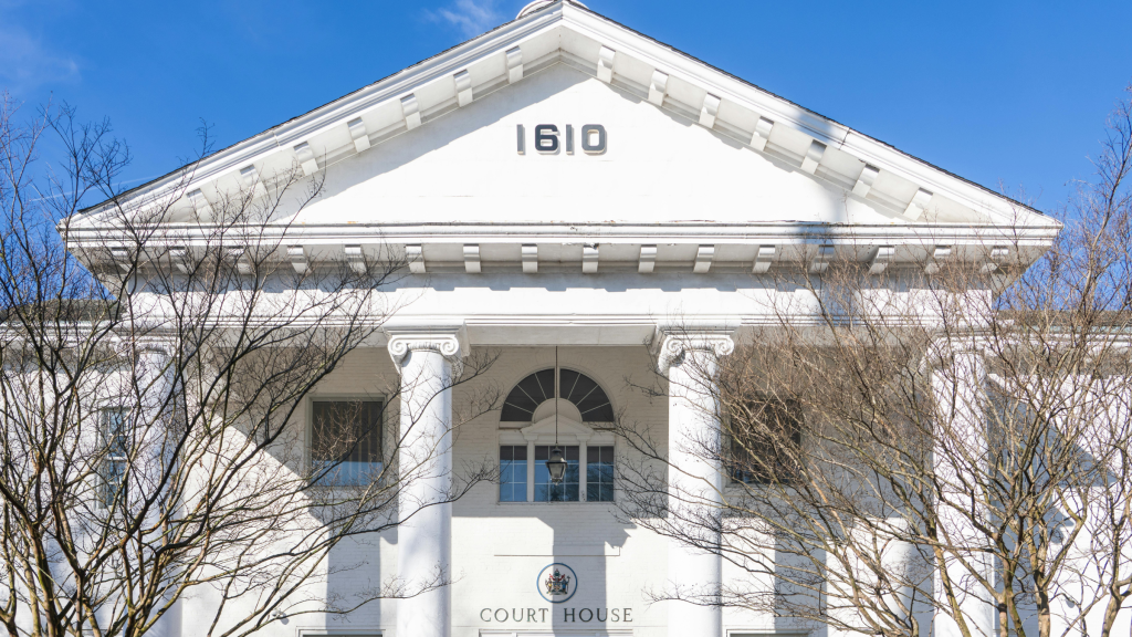 White courthouse building with columns and “1610” inscription above entrance under clear blue sky.