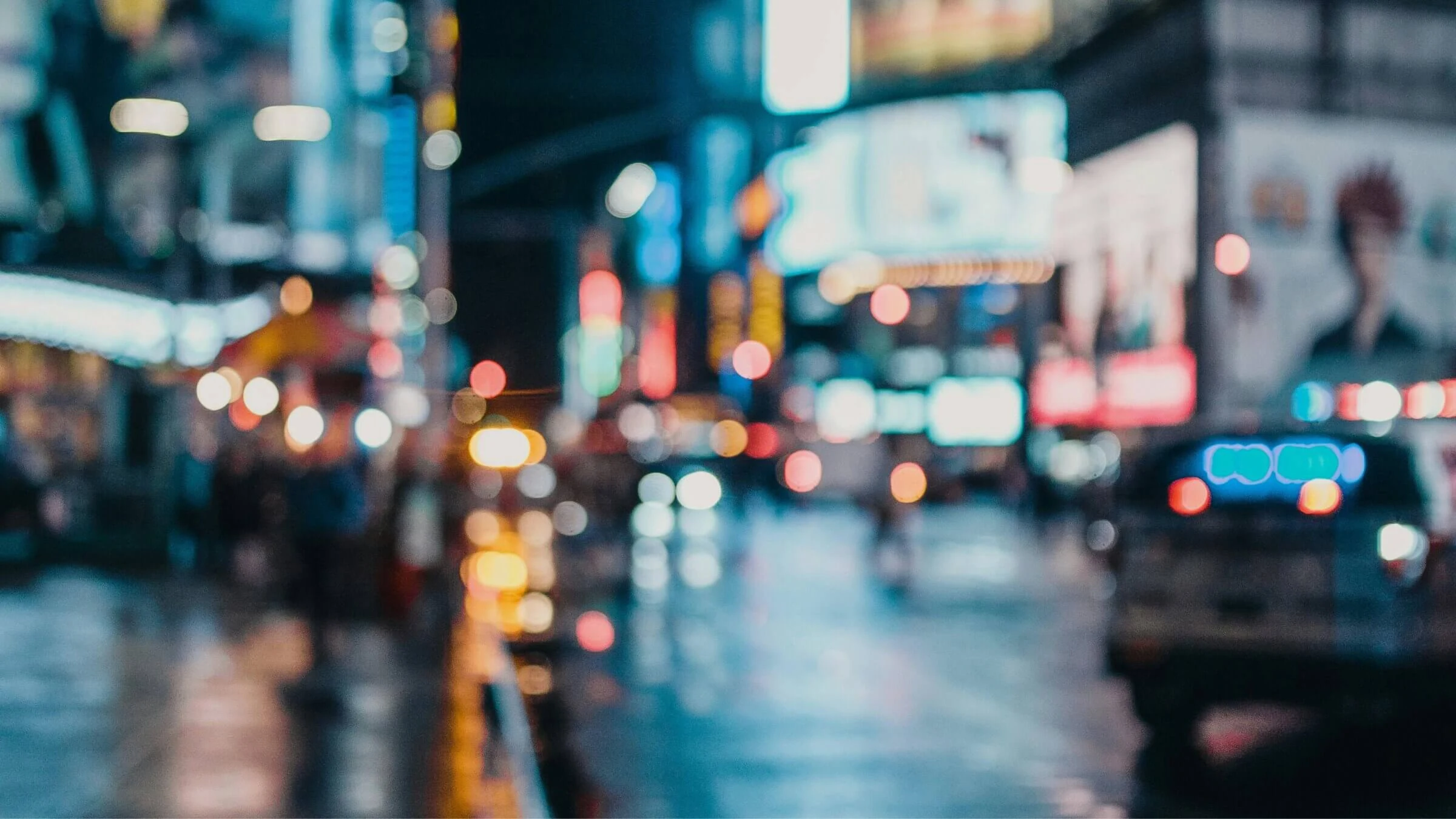 Blurred nighttime city street scene with colorful lights traffic and pedestrians out of focus