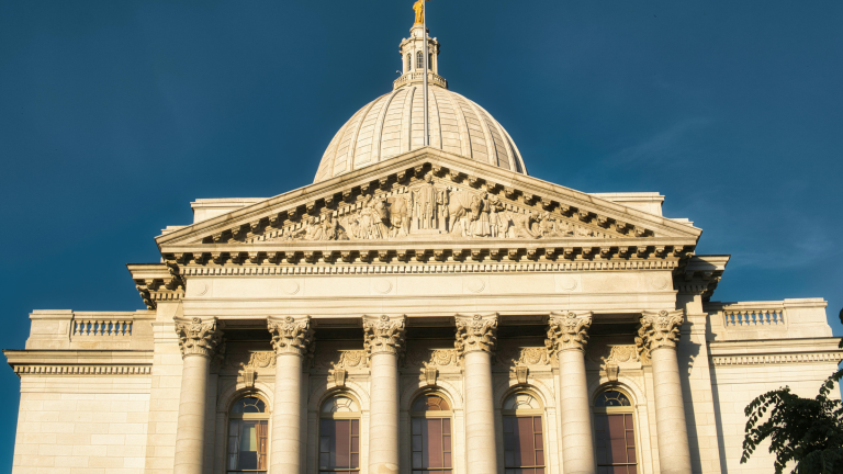 Large domed government building with classical columns and detailed stone carvings under blue sky.